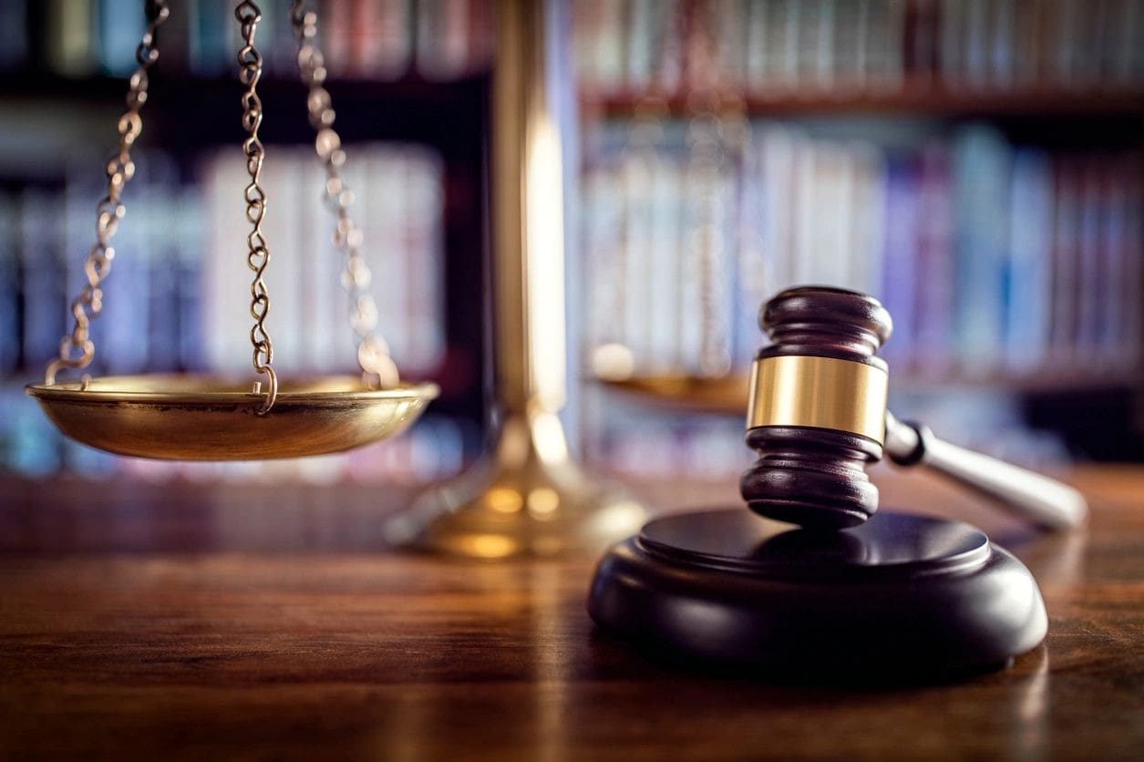 A judge 's gavel and scale in front of a bookshelf.