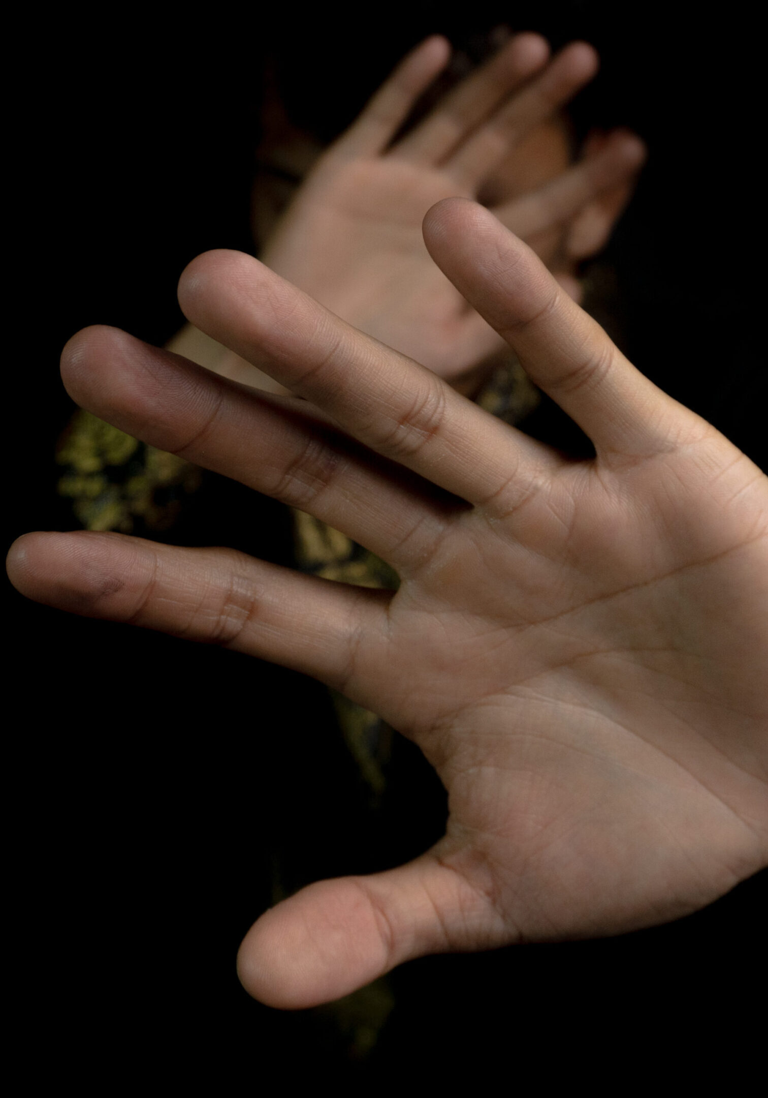 person's hand with palm facing the camera, with the rest of the body blurred in the background trying to defend themselves or to ward something off. The image has a dark and mysterious feel.