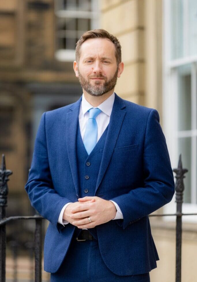 A man in a suit and tie standing next to a fence.